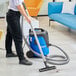 A person using a Nilfisk wet/dry vacuum to clean the floor.