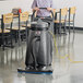 A woman using a Viper Shovelnose wet/dry vacuum to clean a floor in a room with chairs and tables.