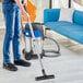 A person using a Nilfisk stainless steel wet / dry vacuum to clean the floor.