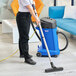 A woman using a Clarke Maxxi II wet / dry vacuum to clean the floor in a room.