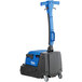 A blue and black Clarke walk behind cylindrical floor scrubber with wheels.
