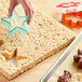 A hand using a star shaped cookie cutter to cut a Kellogg's Rice Krispies Treat sheet.