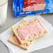A close up of a Pop-Tarts Frosted Cherry Toaster Pastry package on a table with a pair of cherry pastries and a glass of milk.