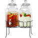 A Stylesetter Rustic Home glass beverage dispenser with two glass jars and lids on a black metal stand filled with a fruity drink.