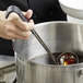 A person using a Vollrath Jacob's Pride ladle with a black handle to stir liquid in a pot.