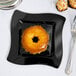 A Fineline black plastic square plate with a pastry on it.