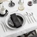 A table setting with a black napkin and Acopa Odin brushed stainless steel demitasse spoons on a table in a fine dining restaurant.