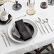 A table set with Acopa Odin stainless steel bouillon spoons, silverware, and a black napkin.