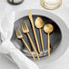 A white plate with an Acopa Odin brushed gold flatware set and a white napkin.