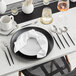 A table set with black and white plates and Acopa Odin brushed stainless steel forks.