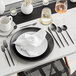 A black table setting with a spoon on a white plate.