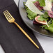 An Acopa Odin brushed stainless steel salad fork on a plate of salad with a napkin.
