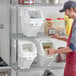 A man in a bakery apron uses a white Baker's Mark ingredient shelf bin to store brown grains.