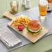 An Acopa faux wood melamine serving board with a burger and fries on a table.