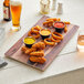 An Acopa walnut faux wood melamine serving board with fried food and sauces on a table.