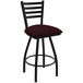 A black Holland Bar Stool ladderback swivel bar stool with a red cushion with black and red stripes.