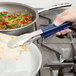 A close-up of a hand holding Vollrath stainless steel tongs with a blue Kool Touch handle.