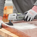 A person using a Genesis oscillating tool to sand a piece of wood.