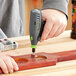 A person using a Genesis 8V Lithium-ion rotary tool to drill holes in a wooden board.