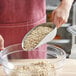 A person using a Choice aluminum scoop to put oats in a bowl.
