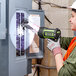 A woman wearing a hard hat and gloves using a green and black PowerSmith spotlight to open an electrical box.