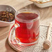 A glass mug of Davidson's Organic Tropical Flower tea next to a bowl of dry tea leaves.
