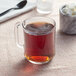 A glass mug of Davidson's Organic Kukicha tea with sugar cubes and a spoon on a white napkin.