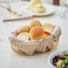 An Acopa oval gold wire basket filled with bread on a table.