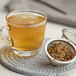 A glass cup of Davidson's Organic Tulsi Spicy Green Loose Leaf Tea with a strainer of herbs.