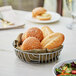 A round chrome wire basket filled with bread rolls and salad on a table.