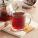 A glass mug of Davidson's Organic Raspberry Essence tea with a spoon on a white surface.