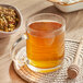 A glass mug of Davidson's Organic Tulsi Chamomile Flower tea next to a bowl of herbs.