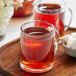 A glass mug of Davidson's Organic Tulsi Hibiscus tea on a wooden tray with sugar cubes.