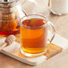 A glass mug of Davidson's Organic White Peony tea with honey on a wooden spoon.