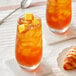 A glass of Davidson's Organic Tropical Iced Tea with ice and an orange slice, next to a croissant.