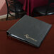 A black leather Menu Solutions reservation binder on a table in a restaurant.