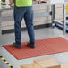 A man standing on a red Choice anti-fatigue floor mat with drainage holes.