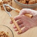 A person using an Acopa stainless steel lobster cracker with a wood handle to crack walnuts.