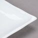 A close-up of a CAC Bamboo Pattern bright white square porcelain plate with a thin rim.