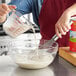 A hand using a whisk to stir California Farms evaporated milk in a bowl.