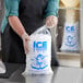 A person in a black apron holding a clear plastic ice bag with "Ice" print.