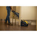 A person using a black and yellow Tornado Vortex walk behind floor scrubber to clean a floor.