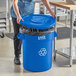 A woman putting a Lavex blue recycling can into a recycle bin.