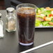 A Cambro clear plastic tumbler filled with soda and ice on a table with a salad.