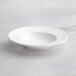 An Acopa Cordelia white porcelain bowl with a wide rim on a marble surface.