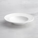 An Acopa Cordelia bright white porcelain bowl with a wide, curved rim on a marble surface.