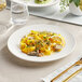 An Acopa Cordelia bright white porcelain plate with embossed wide rim holding pasta with mushrooms and lemon.