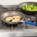 A Vollrath Wear-Ever aluminum non-stick fry pan with a blue Cool Handle filled with chicken and broccoli cooking on a stove.