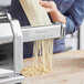 A woman using an Imperia pasta machine to make tagliatelle pasta.