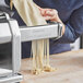 A woman using an Imperia pasta machine to cut noodles.